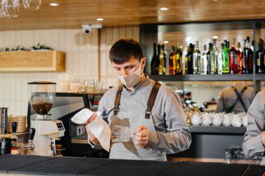 Salgın sırasında maskeli ve üniformalı iki şık barmen, parlamak için gözlük. Salgın sırasında restoranların ve kafelerin çalışmaları.