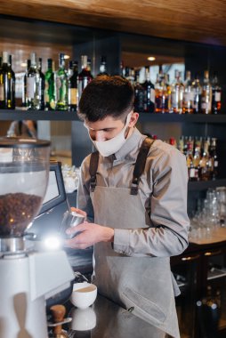 Maskeli bir baristanın bir kafede nefis bir kahve hazırlarken yakın çekimi. Salgın sırasında restoranların ve kafelerin çalışmaları.