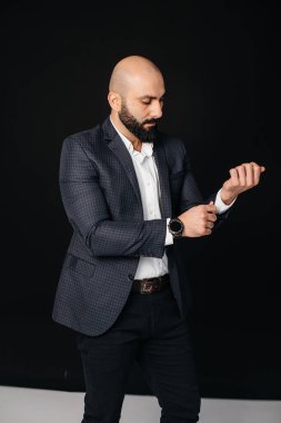 Beyaz gömlekli ve ceketli genç sakallı bir adam siyah arka planda duruyor..