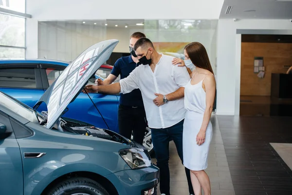 Young couple in masks selects a new vehicle and consult with a representative of the dealership in the period of the pandemic. Car sales, and life during the pandemic