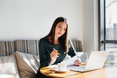 Genç ve güzel bir kız bir kafede oturuyor, bilgisayar başında çalışıyor ve sosyal ağlarda iletişim kuruyor..