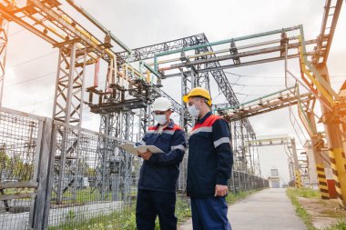 Mühendislerin elektrik santralleri, pandemi zamanında maske içinde modern yüksek voltajlı ekipman araştırması yapar. Enerji. Sanayi