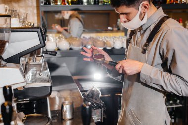 Maskeli bir baristanın bir kafede nefis bir kahve hazırlarken yakın çekimi. Salgın sırasında restoranların ve kafelerin çalışmaları.