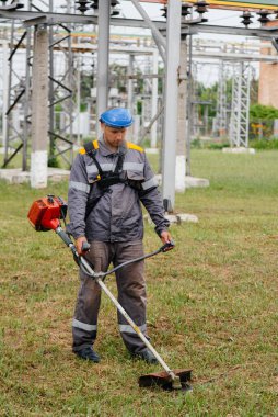 Elektirik santralinin bölgesinde çim biçen genç bir adam. Girişimdeki çim temizleme, yangın güvenlik önlemlerinin uygulanması