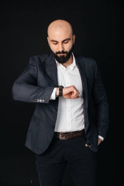 Beyaz gömlekli ve ceketli genç sakallı bir adam siyah arka planda duruyor..