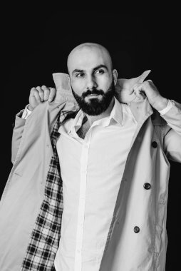 Genç sakallı bir adam siyah bir arka plana karşı yağmurluğunu ayarlar. Siyah ve beyaz.