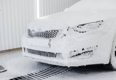 Köpüklü modern yıkama ve beyaz bir arabanın yüksek basınçlı suyu. Araba yıkama