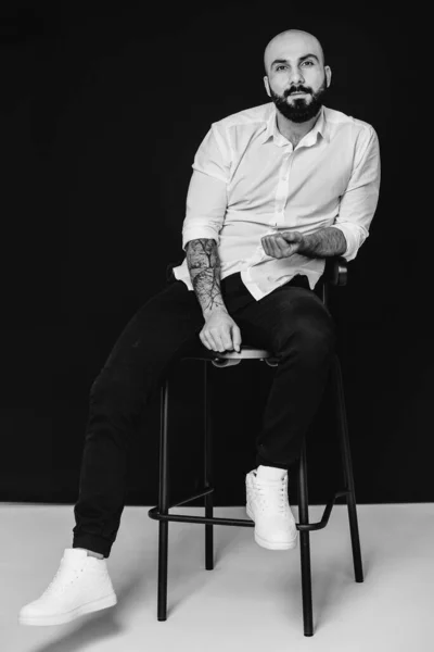 白いシャツを着た若い髭の男が黒い背景に腰を下ろしている 黒と白 — ストック写真