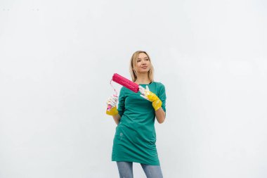 Genç bir kız beyaz bir duvar boyamadan önce pembe bir silindirle poz veriyor. İç kısmın tamiri.