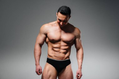 Genç bir sporcu stüdyoda üstsüz poz veriyor, kaslarını ve kaslarını gösteriyor. Spor..