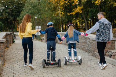 Büyük mutlu bir aile, gün batımında sıcak bir sonbahar gününde Segways ve elektrikli scooter kullanır. Park 'ta aile tatili.