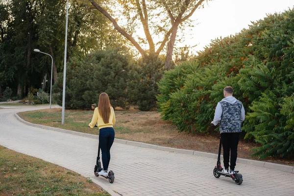 若い美しいカップルは 暖かい秋の日に公園の電動スクーターに乗っています 趣味とレクリエーション — ストック写真