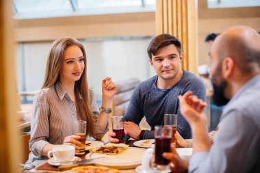 Bir grup neşeli genç arkadaş bir kafede oturmuş konuşuyor ve pizza yiyorlar. Pizzacıda öğle yemeği..