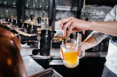 Barmenin bir bardak light birayı doldurduğu yakın plan fotoğraf. Bardaki bar tezgahı..