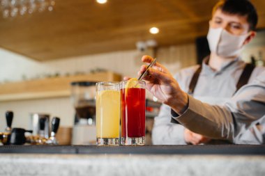 Salgın sırasında maskeli ve üniformalı iki şık barmen kokteyl hazırlıyor. Salgın sırasında restoranların ve kafelerin çalışmaları.