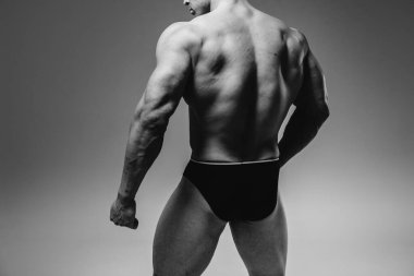 Genç bir sporcu stüdyoda üstsüz poz veriyor, kaslarını ve kaslarını gösteriyor. Siyah ve beyaz.
