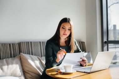 Genç ve güzel bir kız bir kafede oturuyor, bilgisayar başında çalışıyor ve sosyal ağlarda iletişim kuruyor..