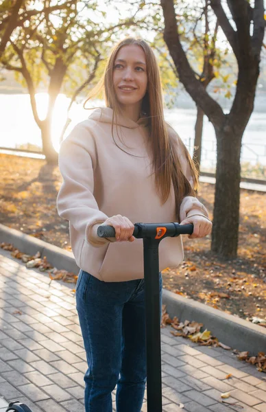 暖かい秋の日に電気スクーターで公園に乗る若い美しい女の子 — ストック写真