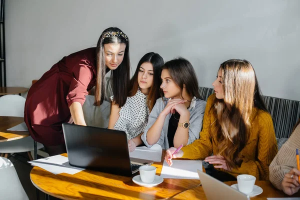 A group of young girls sit in an office at computers and discuss projects. Communication and training online.