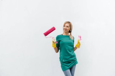 Genç bir kız beyaz bir duvar boyamadan önce pembe bir silindirle poz veriyor. İç kısmın tamiri.