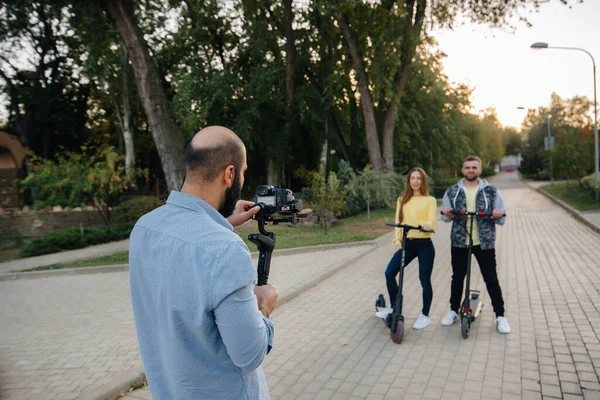 They shoot a video blog about a young beautiful couple riding electric scooters in a Park on a warm autumn day. Hobbies and recreation.