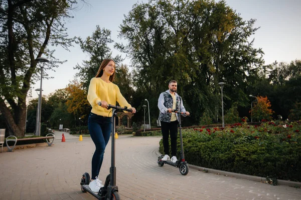 若い美しいカップルは 暖かい秋の日に公園の電動スクーターに乗っています 趣味とレクリエーション — ストック写真