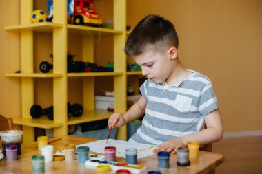 Odasında küçük sevimli bir çocuk oynuyor ve resim yapıyor. Eğlence ve eğlence. Evde kal.