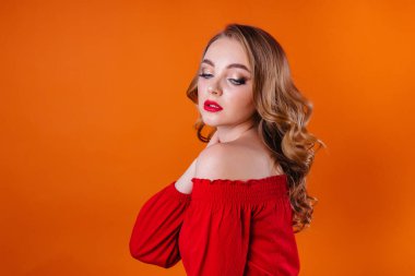 Genç ve güzel bir kız duygularını gösterir ve stüdyoda turuncu bir arka planda gülümser. Reklam için kızlar