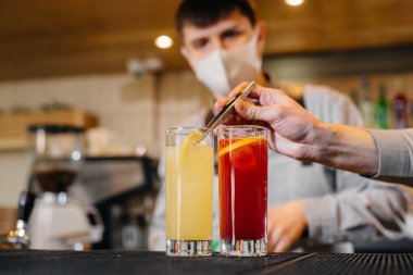 Salgın sırasında maskeli ve üniformalı iki şık barmen kokteyl hazırlıyor. Salgın sırasında restoranların ve kafelerin çalışmaları.