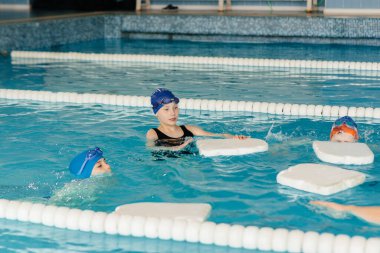 Bir grup kız ve erkek, bir eğitmenle havuzda yüzmeyi öğreniyor. Çocuk sporlarının gelişimi.