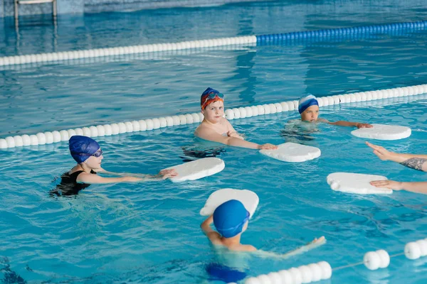 A group of boys and girls train and learn to swim in the pool with an instructor. Development of children\'s sports.