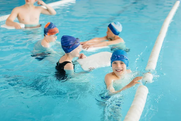 A group of boys and girls train and learn to swim in the pool with an instructor. Development of children\'s sports.