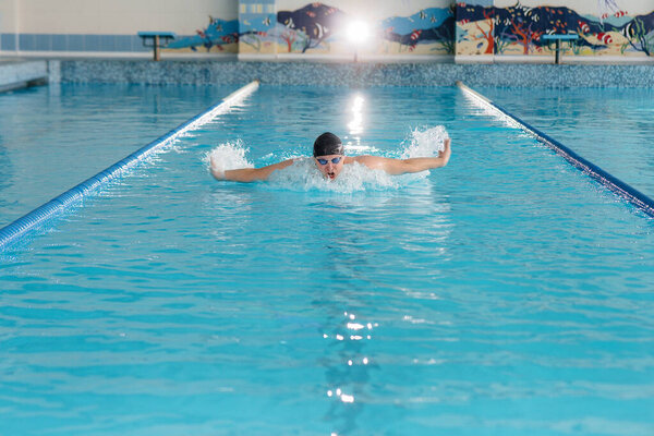 Молодой атлет тренируется и готовится к соревнованиям по плаванию в бассейне. Здоровый образ жизни.