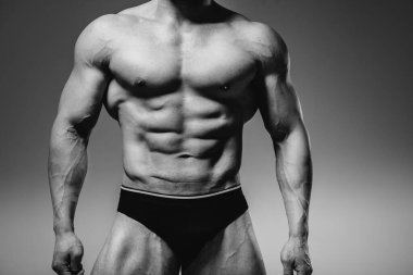 Genç bir sporcu stüdyoda üstsüz poz veriyor, kaslarını ve kaslarını gösteriyor. Siyah ve beyaz.