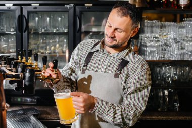 Bir bardak bira dolduran sakallı bir barmenin yakın çekimi. Bardaki bar tezgahı..