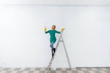 Merdivendeki genç bir kız beyaz bir duvarı silindirle boyuyor. İç kısmın tamiri.