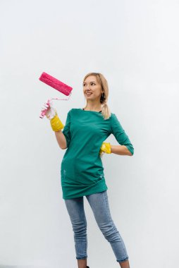 Genç bir kız beyaz bir duvar boyamadan önce pembe bir silindirle poz veriyor. İç kısmın tamiri.