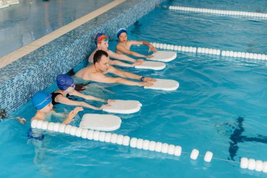 Bir grup kız ve erkek, bir eğitmenle havuzda yüzmeyi öğreniyor. Çocuk sporlarının gelişimi.