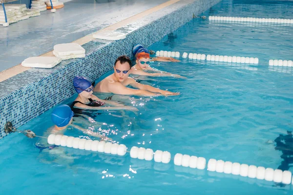A group of boys and girls train and learn to swim in the pool with an instructor. Development of children\'s sports.