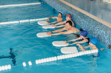 Bir grup kız ve erkek, bir eğitmenle havuzda yüzmeyi öğreniyor. Çocuk sporlarının gelişimi.