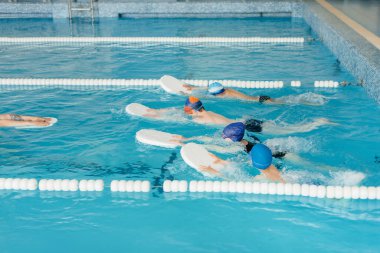 Bir grup kız ve erkek, bir eğitmenle havuzda yüzmeyi öğreniyor. Çocuk sporlarının gelişimi.