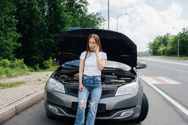 一个年轻的女孩站在高速公路中央一辆抛锚的汽车旁边 打电话求助 汽车故障和抛锚 等人帮忙 — 图库照片