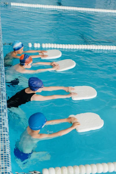 A group of boys and girls train and learn to swim in the pool with an instructor. Development of children's sports.