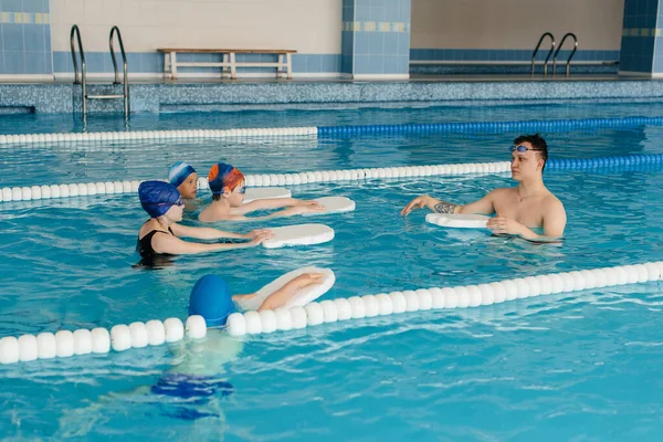 A group of boys and girls train and learn to swim in the pool with an instructor. Development of children's sports.