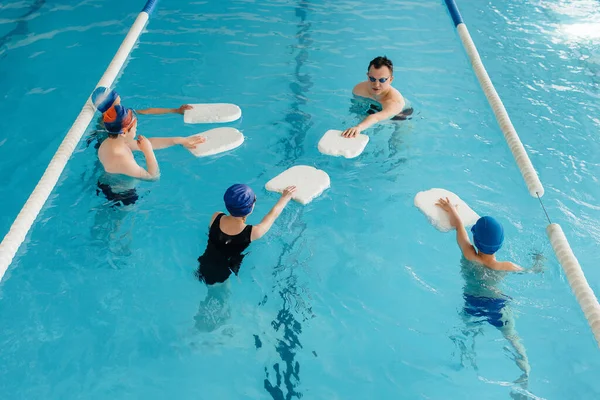 A group of boys and girls train and learn to swim in the pool with an instructor. Development of children's sports.