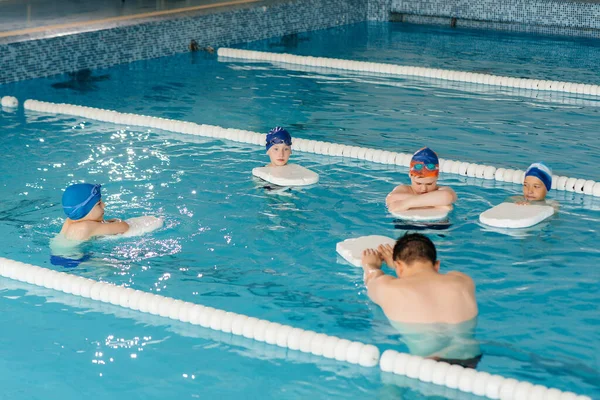 A group of boys and girls train and learn to swim in the pool with an instructor. Development of children\'s sports.