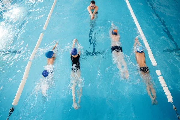 A group of boys and girls train and learn to swim in the pool with an instructor. Development of children\'s sports.