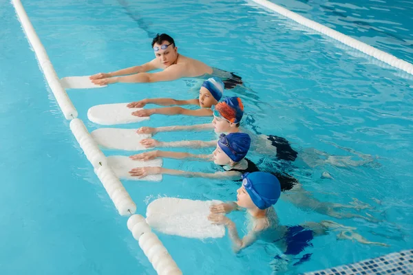 A group of boys and girls train and learn to swim in the pool with an instructor. Development of children\'s sports.