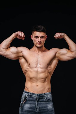 Mükemmel karın kasları olan genç seksi bir sporcu arka planda kot pantolonla stüdyoda üstsüz poz veriyor. Sağlıklı yaşam tarzı, düzgün beslenme, eğitim programları ve kilo vermek için beslenme.