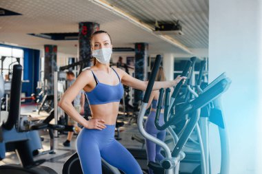 Salgın sırasında maske takan iki güzel kız spor salonunda egzersiz yapıyor. Halka açık yerlerde sosyal mesafeler.